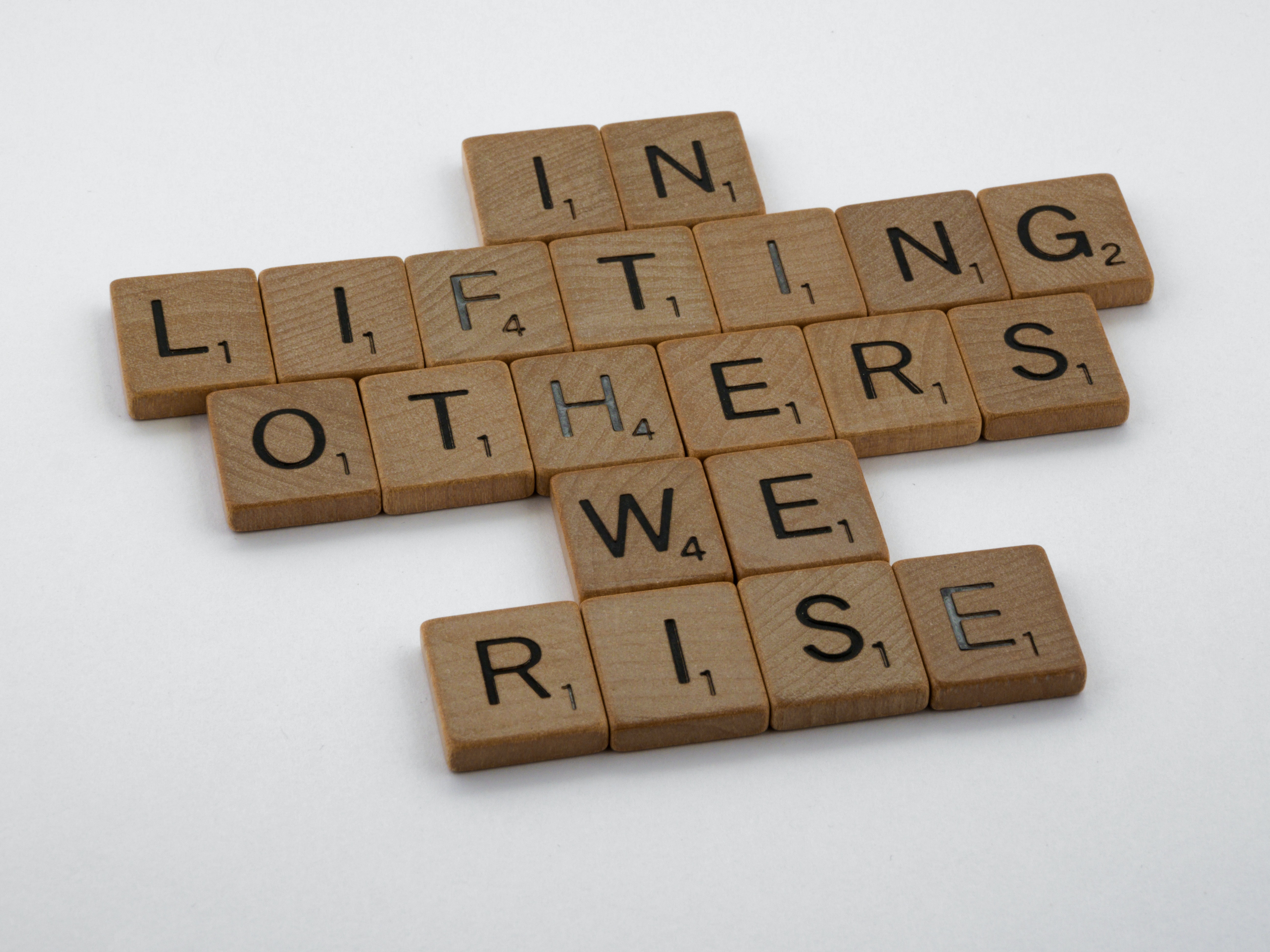 Scrabble Pieces making the words:  In lifting others we rise