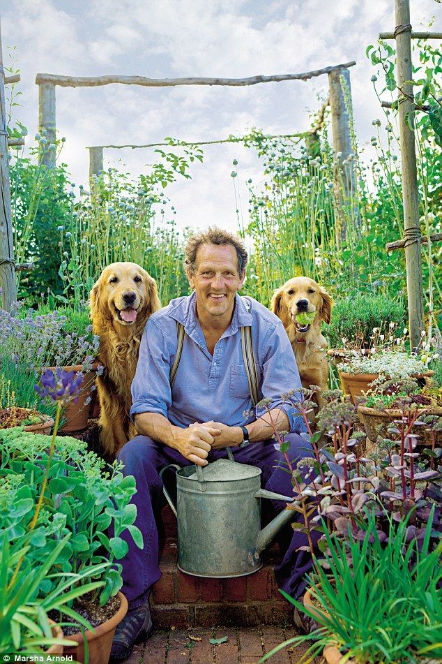 British gardening guru Monty Don holding a watering can in his garden with his 2 golden retrievers at his side