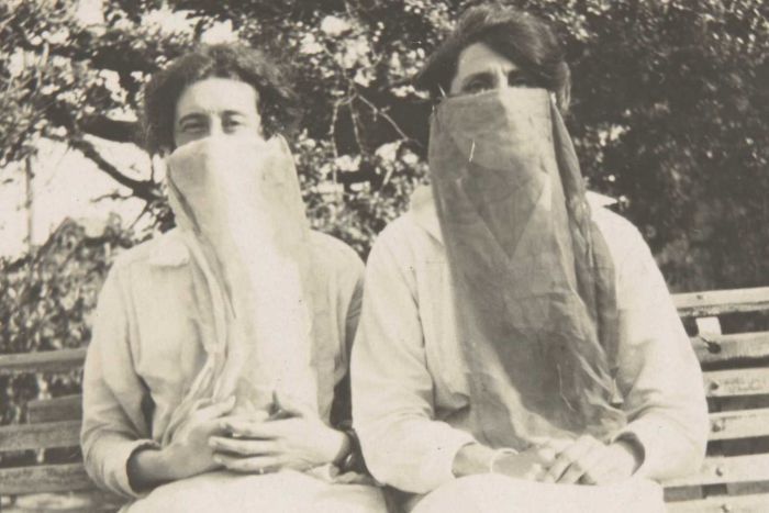 sepia tone photo of two women sitting on a bench wearing cloth masks circa 1918