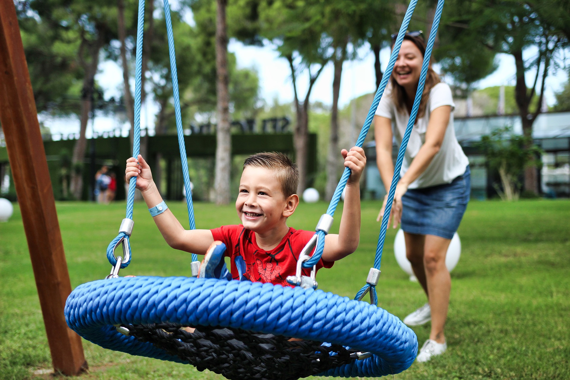 Smiling son on round web swing being pushed by his mother
