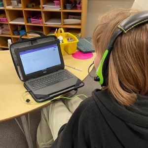 Third grader wearing headphones with a mic sitting in front of a computer with a document open.